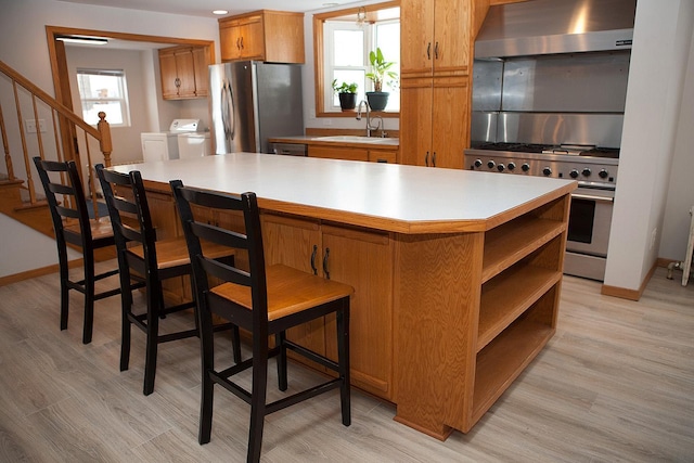 kitchen with appliances with stainless steel finishes, washer / dryer, a kitchen island, wall chimney range hood, and a breakfast bar