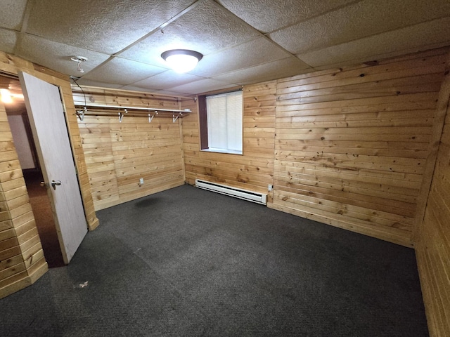 empty room featuring a baseboard heating unit, wooden walls, and dark carpet