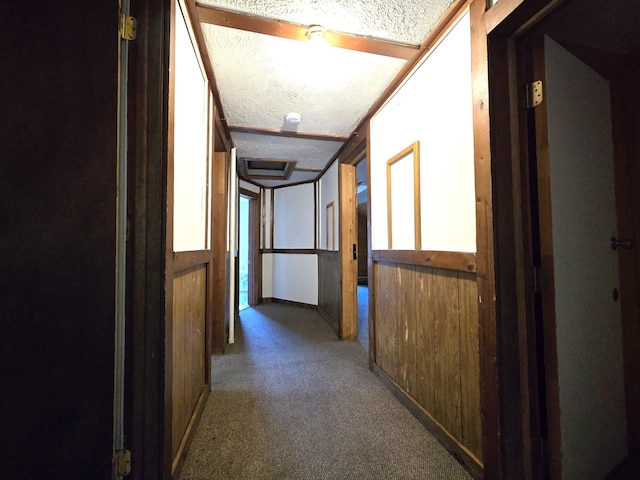 hallway with a textured ceiling, wood walls, and carpet flooring