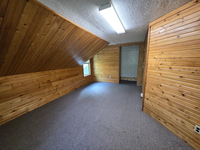 bonus room with a textured ceiling, wooden walls, lofted ceiling, dark colored carpet, and wooden ceiling