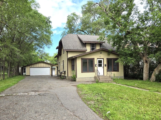 bungalow featuring a front lawn, a garage, and an outbuilding