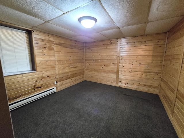 unfurnished room with a paneled ceiling, a baseboard heating unit, wooden walls, and carpet flooring