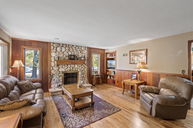 living area with wooden walls, light wood finished floors, a fireplace, and a wainscoted wall