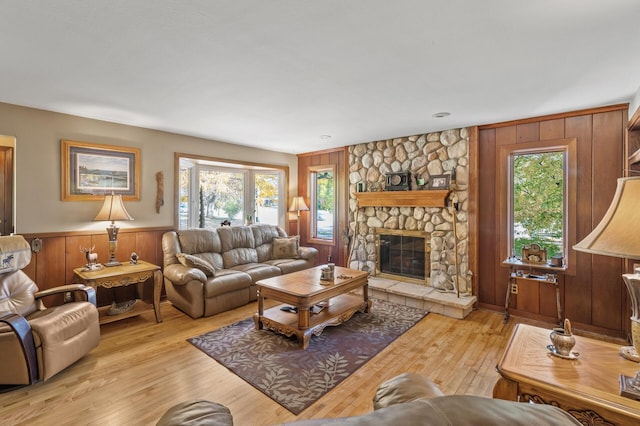 living room featuring healthy amount of natural light, light wood finished floors, a stone fireplace, wooden walls, and wainscoting