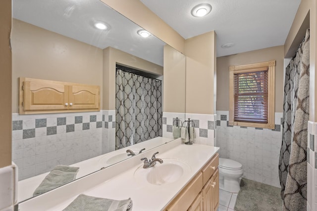 full bathroom featuring tile walls, a wainscoted wall, tile patterned floors, toilet, and vanity