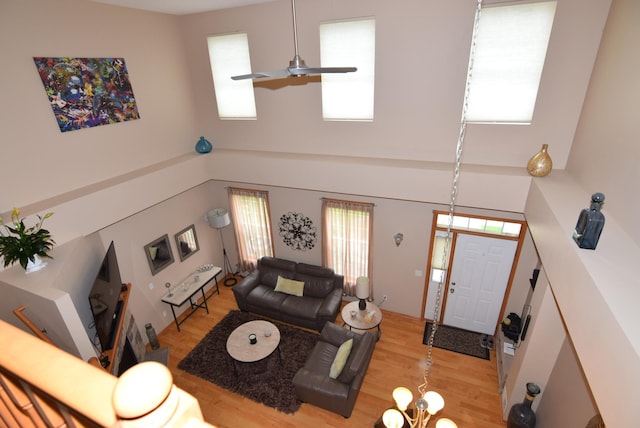 living room featuring light hardwood / wood-style floors, a towering ceiling, and ceiling fan with notable chandelier