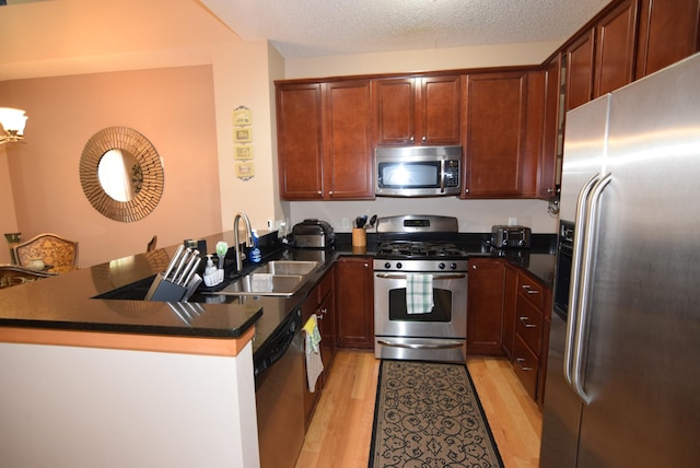 kitchen with appliances with stainless steel finishes, kitchen peninsula, a textured ceiling, light hardwood / wood-style flooring, and sink