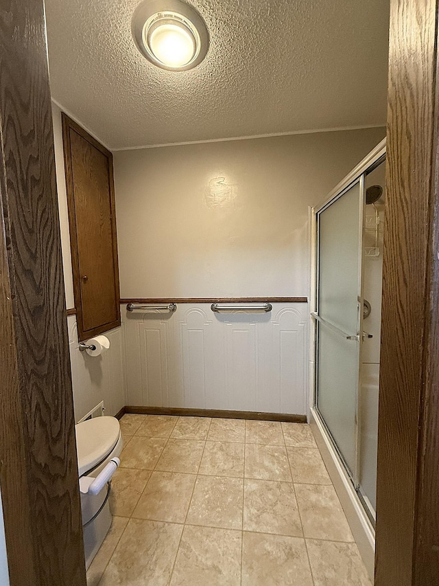 619 10th St, Montevideo, MN 56265 - full bath with a textured ceiling, a shower stall, toilet, a wainscoted wall, and tile patterned floors