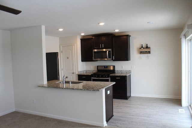 kitchen featuring kitchen peninsula, sink, stainless steel appliances, dark brown cabinets, and light stone counters