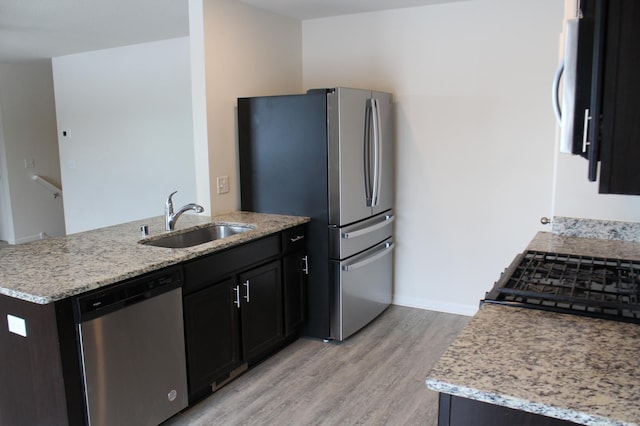 kitchen featuring appliances with stainless steel finishes, light hardwood / wood-style flooring, light stone counters, and sink