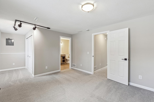 spare room featuring electric panel, rail lighting, light carpet, and a textured ceiling