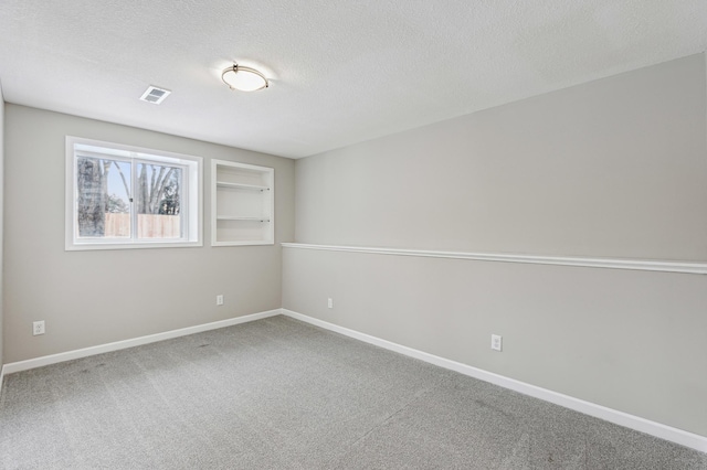 spare room featuring built in shelves, a textured ceiling, and carpet flooring