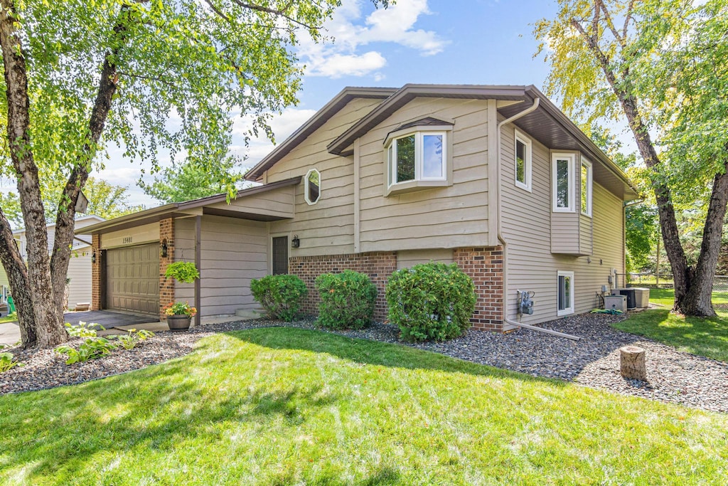 tri-level home featuring central air condition unit, a front yard, and a garage