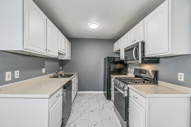 kitchen with white cabinets, appliances with stainless steel finishes, marble finish floor, light countertops, and a sink