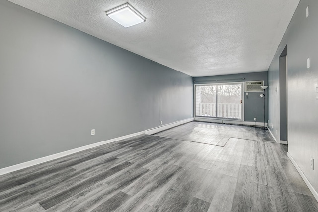 unfurnished room with a textured ceiling, a wall unit AC, a baseboard radiator, wood finished floors, and baseboards