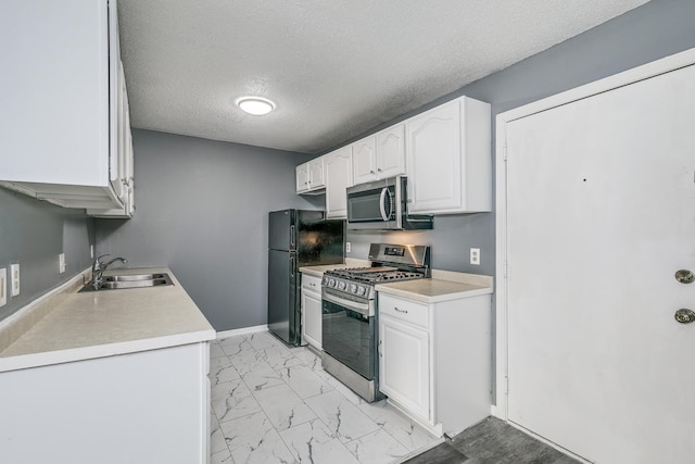 kitchen featuring appliances with stainless steel finishes, marble finish floor, light countertops, white cabinetry, and a sink