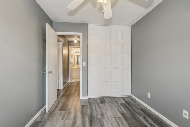 unfurnished bedroom with baseboards, ceiling fan, dark wood-type flooring, a textured ceiling, and a closet