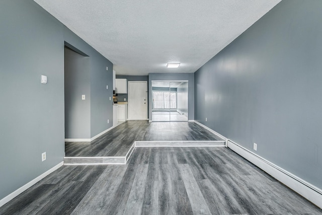 spare room featuring a textured ceiling, dark wood-style flooring, baseboard heating, and baseboards