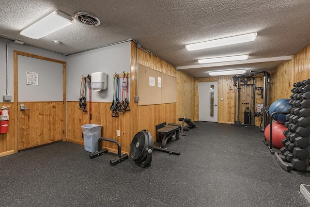 workout area with wooden walls, a wainscoted wall, visible vents, and a textured ceiling