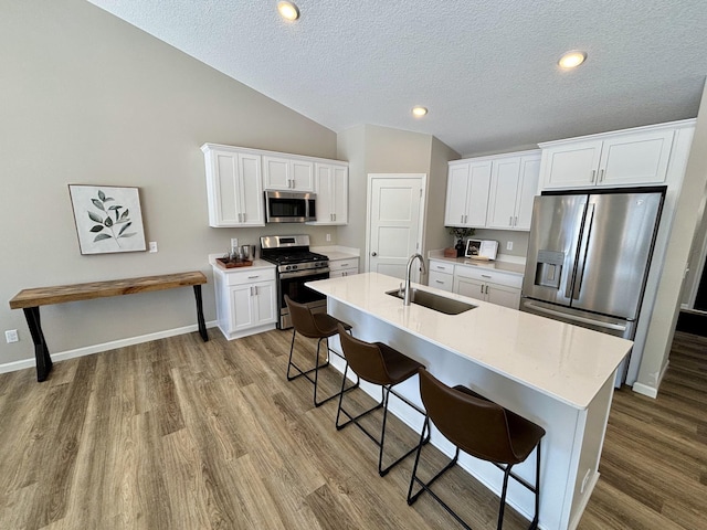 kitchen with a breakfast bar area, a sink, white cabinets, light countertops, and appliances with stainless steel finishes