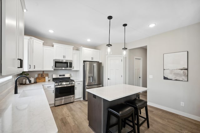 kitchen with sink, appliances with stainless steel finishes, white cabinetry, a center island, and decorative light fixtures