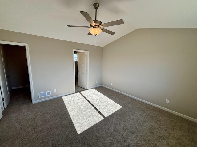 unfurnished bedroom with vaulted ceiling, a walk in closet, ceiling fan, and dark carpet