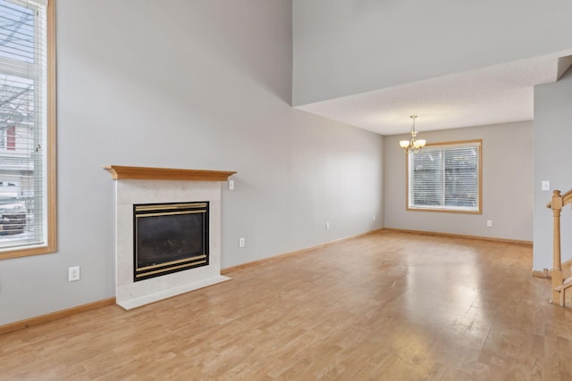 unfurnished living room with light wood-type flooring, a healthy amount of sunlight, and an inviting chandelier