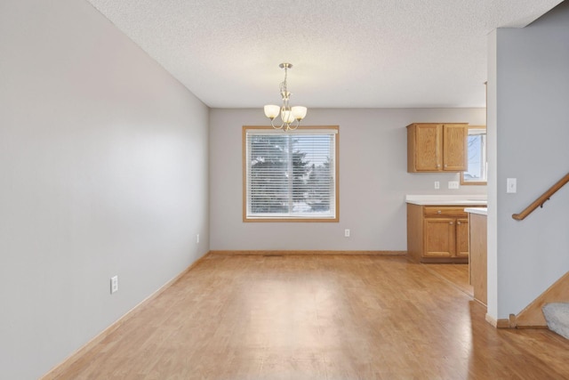 unfurnished dining area featuring an inviting chandelier, a textured ceiling, and light wood-type flooring