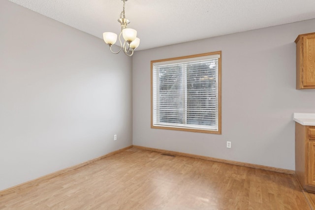 unfurnished dining area featuring a textured ceiling, an inviting chandelier, and light hardwood / wood-style flooring