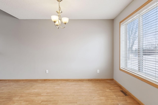 spare room featuring light wood-type flooring and an inviting chandelier