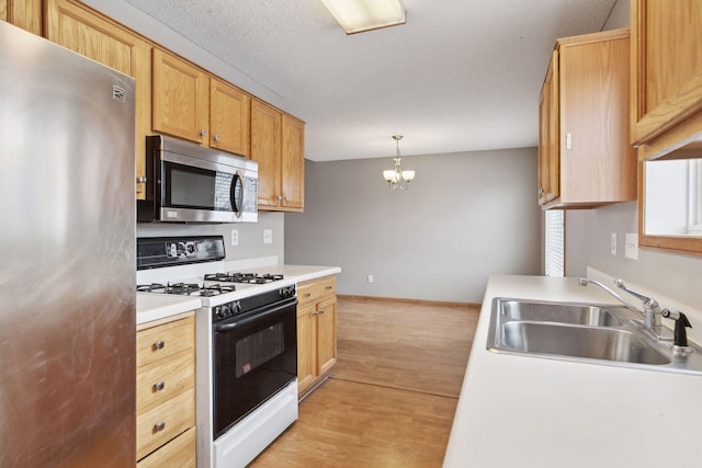 kitchen with pendant lighting, stainless steel appliances, light hardwood / wood-style floors, sink, and a notable chandelier