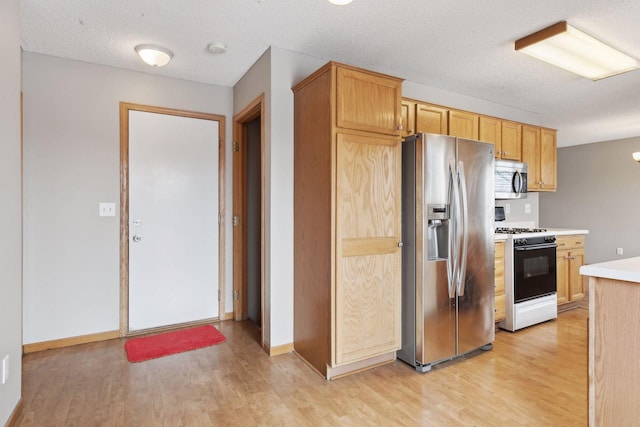 kitchen with light wood-type flooring, stainless steel appliances, a textured ceiling, and light brown cabinets