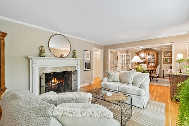 living room featuring a tile fireplace, crown molding, and light hardwood / wood-style floors