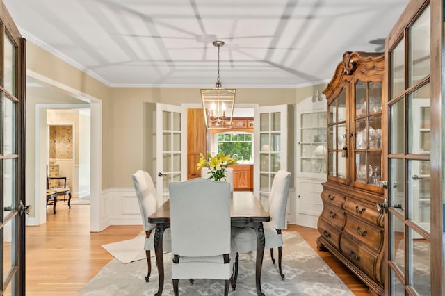 dining area with light hardwood / wood-style flooring, ornamental molding, french doors, and an inviting chandelier