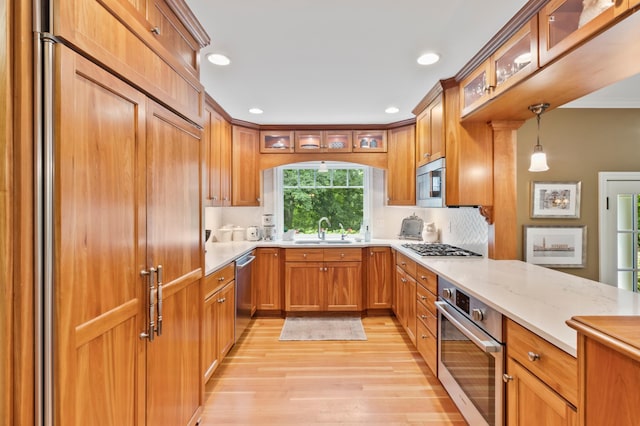 kitchen featuring appliances with stainless steel finishes, decorative light fixtures, decorative backsplash, sink, and light hardwood / wood-style floors