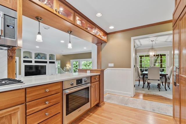 kitchen featuring hanging light fixtures, light wood-type flooring, light stone countertops, stainless steel appliances, and ornamental molding