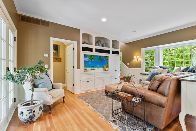 living room with built in features, crown molding, and light wood-type flooring