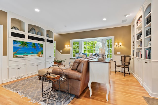 living room with built in shelves, ornamental molding, and light hardwood / wood-style flooring