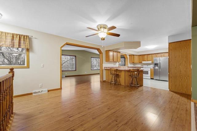 kitchen with light hardwood / wood-style floors, kitchen peninsula, stainless steel refrigerator with ice dispenser, a breakfast bar area, and white range oven