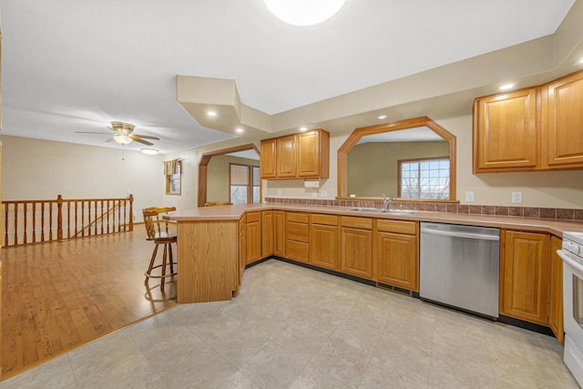 kitchen featuring a kitchen bar, sink, kitchen peninsula, ceiling fan, and stainless steel dishwasher