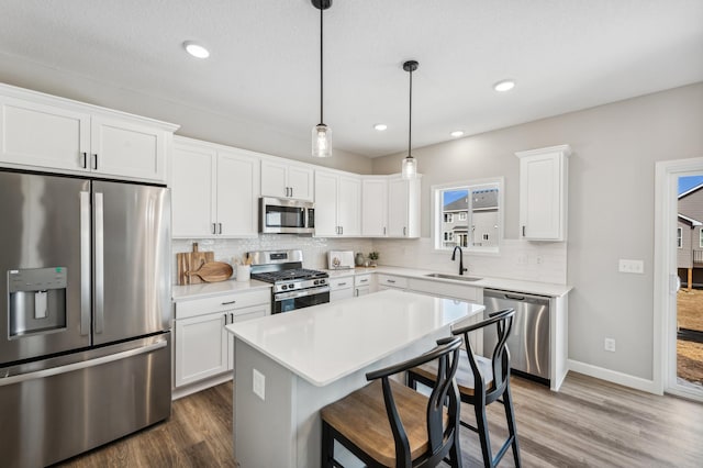 kitchen with pendant lighting, white cabinets, appliances with stainless steel finishes, a center island, and sink