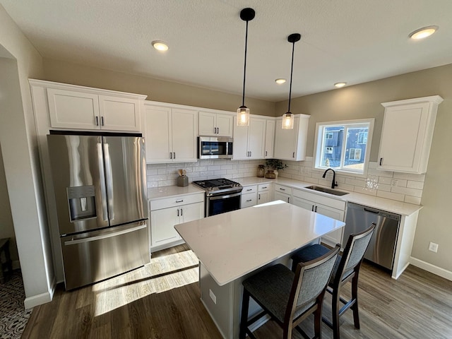 kitchen featuring white cabinetry, stainless steel appliances, a center island, sink, and pendant lighting