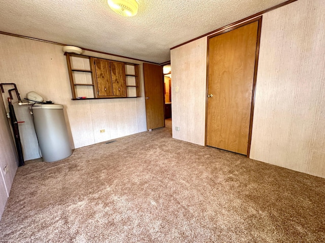 carpeted spare room featuring a textured ceiling, crown molding, and water heater