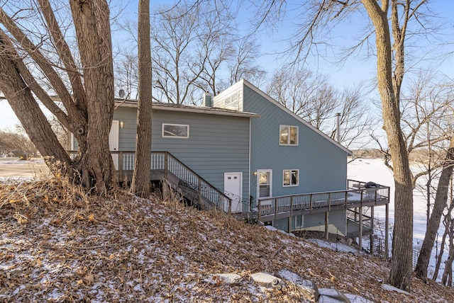 snow covered property featuring a deck, stairway, and a chimney