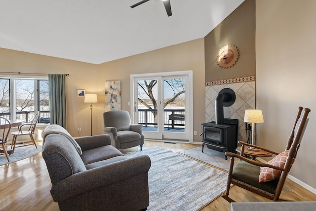 living area with baseboards, a wood stove, ceiling fan, vaulted ceiling, and light wood-type flooring