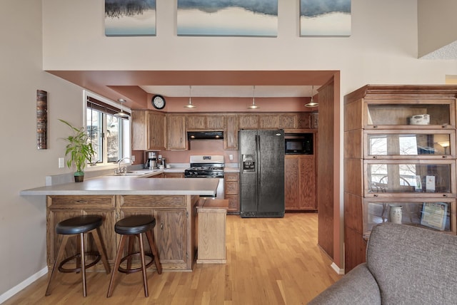 kitchen featuring under cabinet range hood, stainless steel range with gas stovetop, black fridge, a peninsula, and brown cabinetry