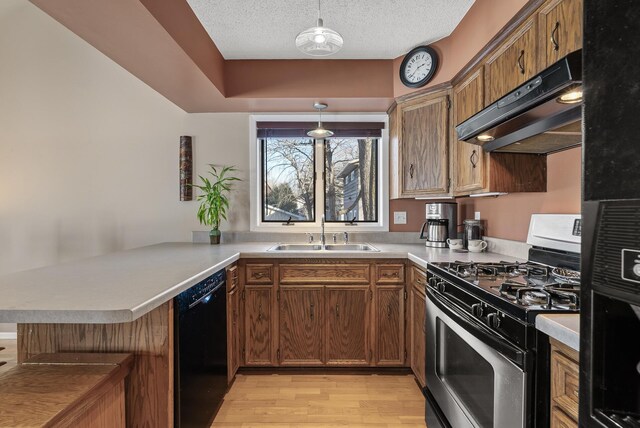 kitchen featuring under cabinet range hood, stainless steel range with gas stovetop, black dishwasher, a peninsula, and a sink