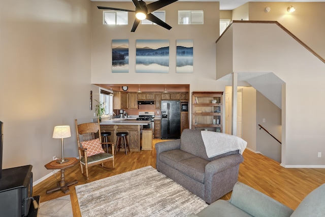 living room featuring a high ceiling, light wood-type flooring, and ceiling fan