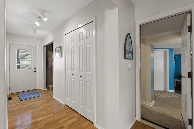 entryway with light wood-style flooring, rail lighting, a textured ceiling, and baseboards