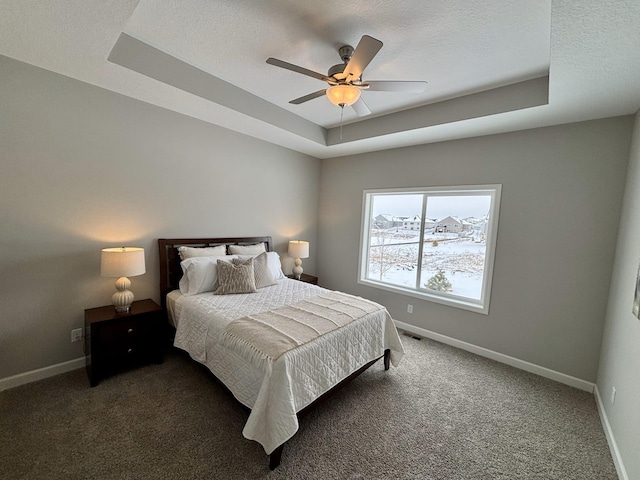 carpeted bedroom with ceiling fan, a tray ceiling, and a textured ceiling